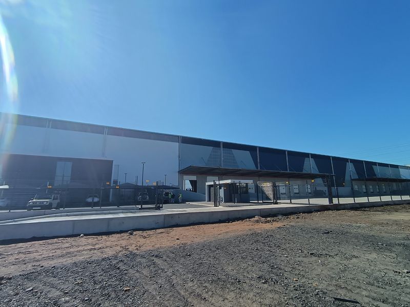 A modern industrial warehouse facility featuring a large facade, integrated loading bays, and a dedicated security gatehouse, set within a secure perimeter.