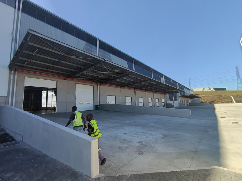 Industrial warehouse exterior featuring multiple loading docks with roller shutter doors, a large concrete yard, and an extensive overhead metal canopy.
