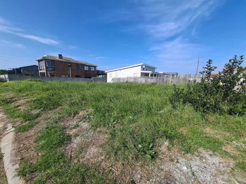 A vacant residential plot featuring grass coverage, enclosed by a combination of concrete boundary walls and timber fencing in a developed neighborhood.