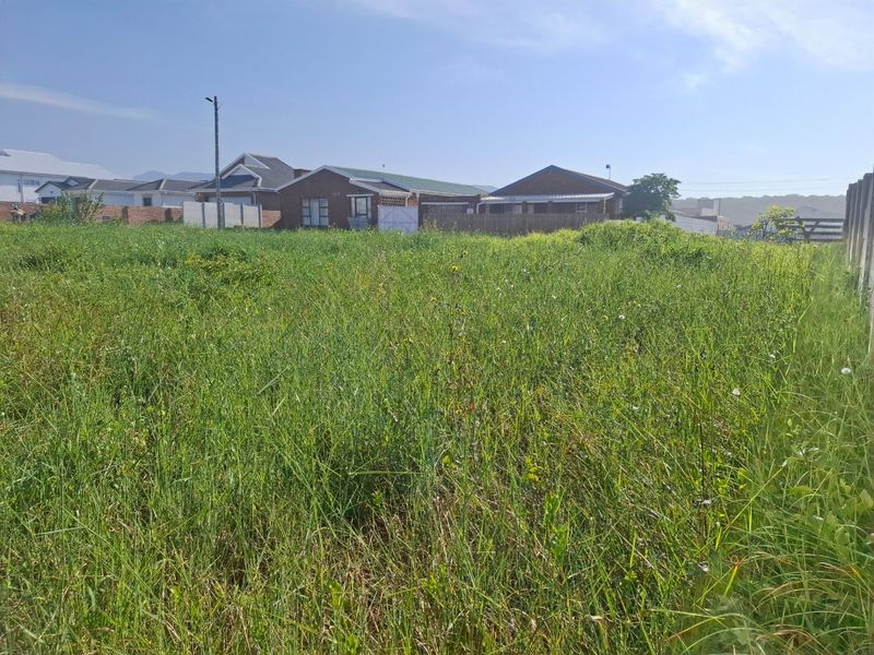 A vacant residential plot covered in tall grass, featuring boundary fencing and a utility pole, situated in a developed neighborhood.