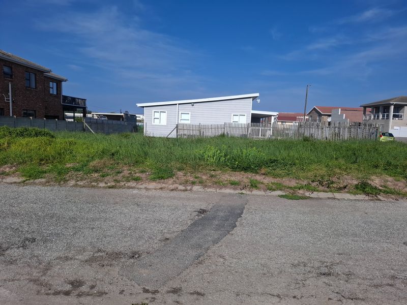 A view of a vacant residential plot from the street, featuring an asphalt road frontage and existing boundary fencing.