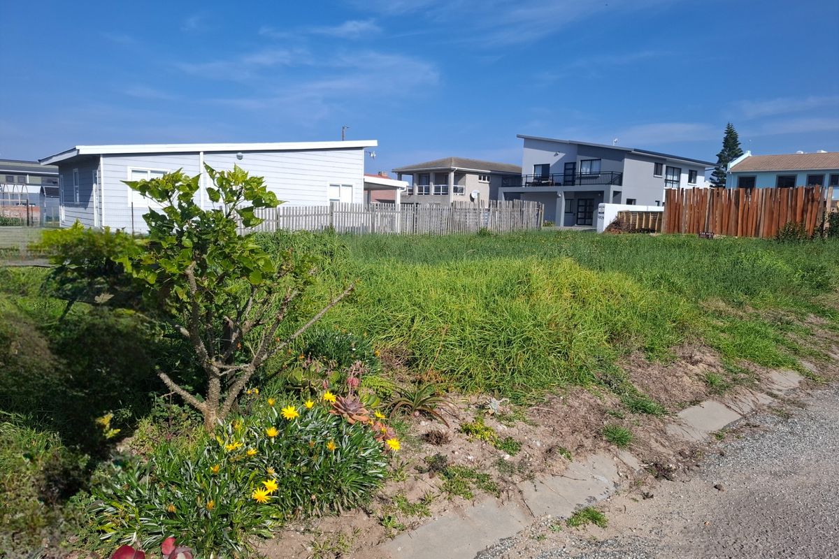 A vacant residential plot featuring overgrown grass and established timber fencing, situated in a developed neighbourhood with paved street access.