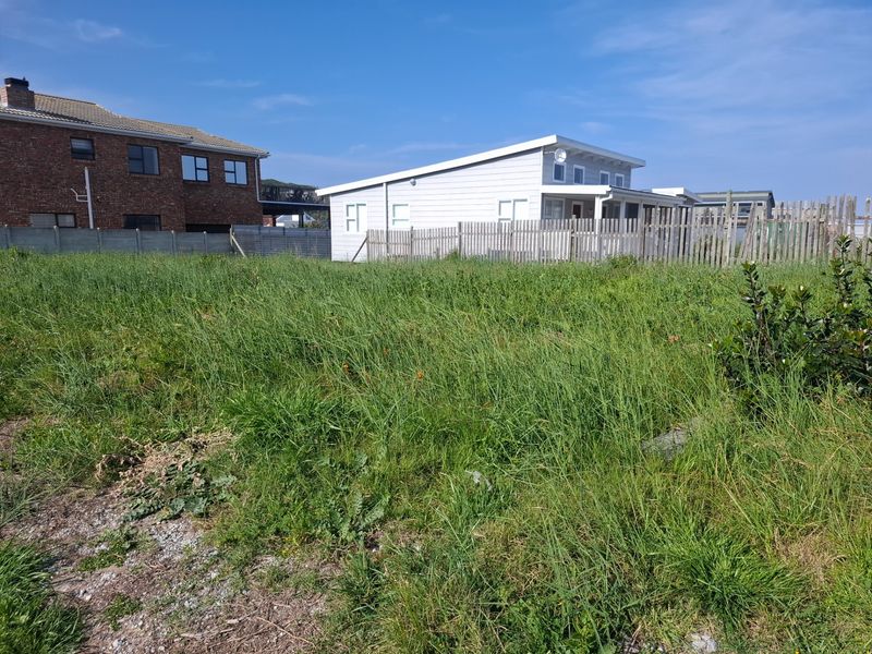 A vacant residential plot featuring overgrown grass and boundary fencing, situated in a developed neighborhood setting.