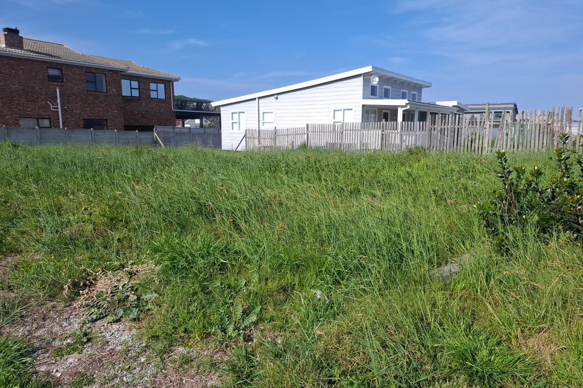 A vacant residential plot featuring overgrown grass and boundary fencing, situated in a developed neighborhood setting.