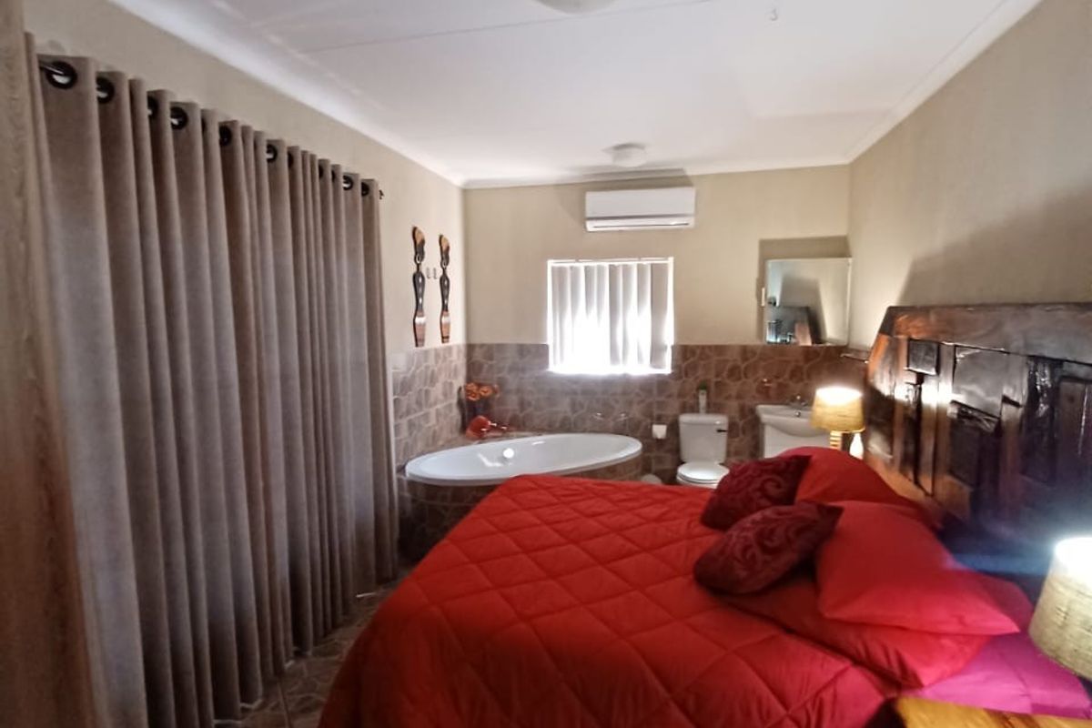 A bedroom featuring an open-plan layout with an integrated bathtub and toilet, tiled flooring, and a wall-mounted air conditioning unit.
