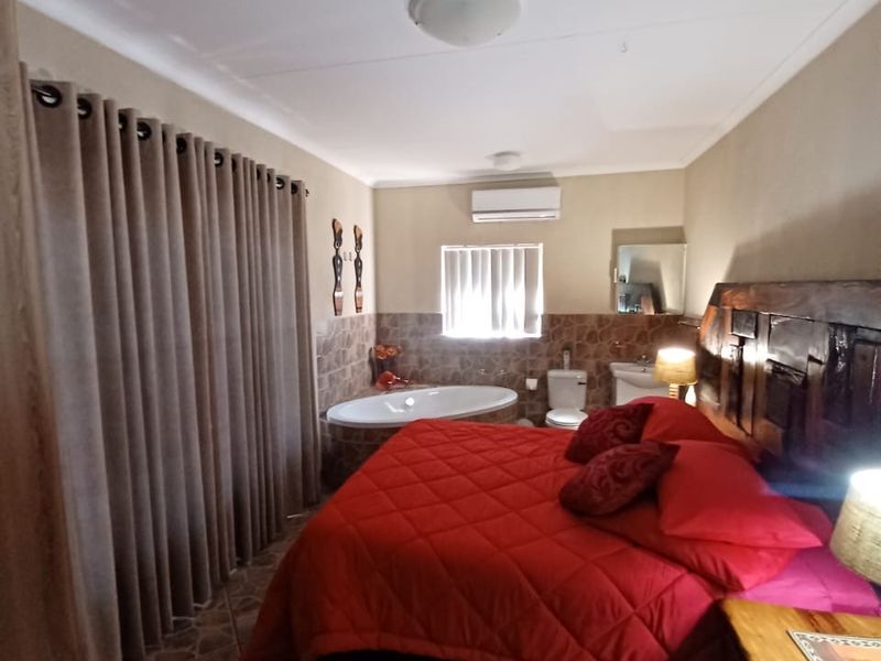 A bedroom featuring an open-plan layout with an integrated bathtub and toilet, tiled flooring, and a wall-mounted air conditioning unit.
