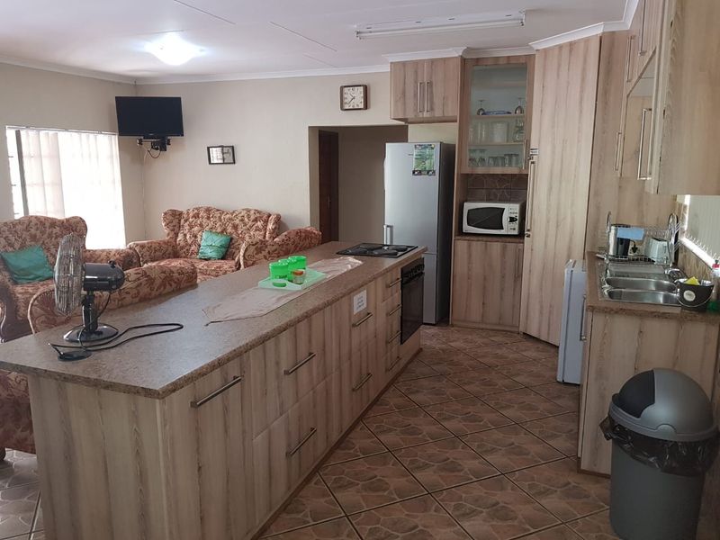 Open-plan kitchen and living area featuring wood-look cabinetry, a central island with integrated hob, and tiled flooring throughout.
