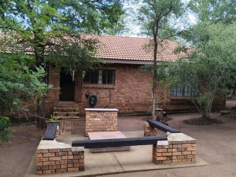 Rear exterior view of a brick house featuring a built-in brick braai and integrated seating area set within a garden space.
