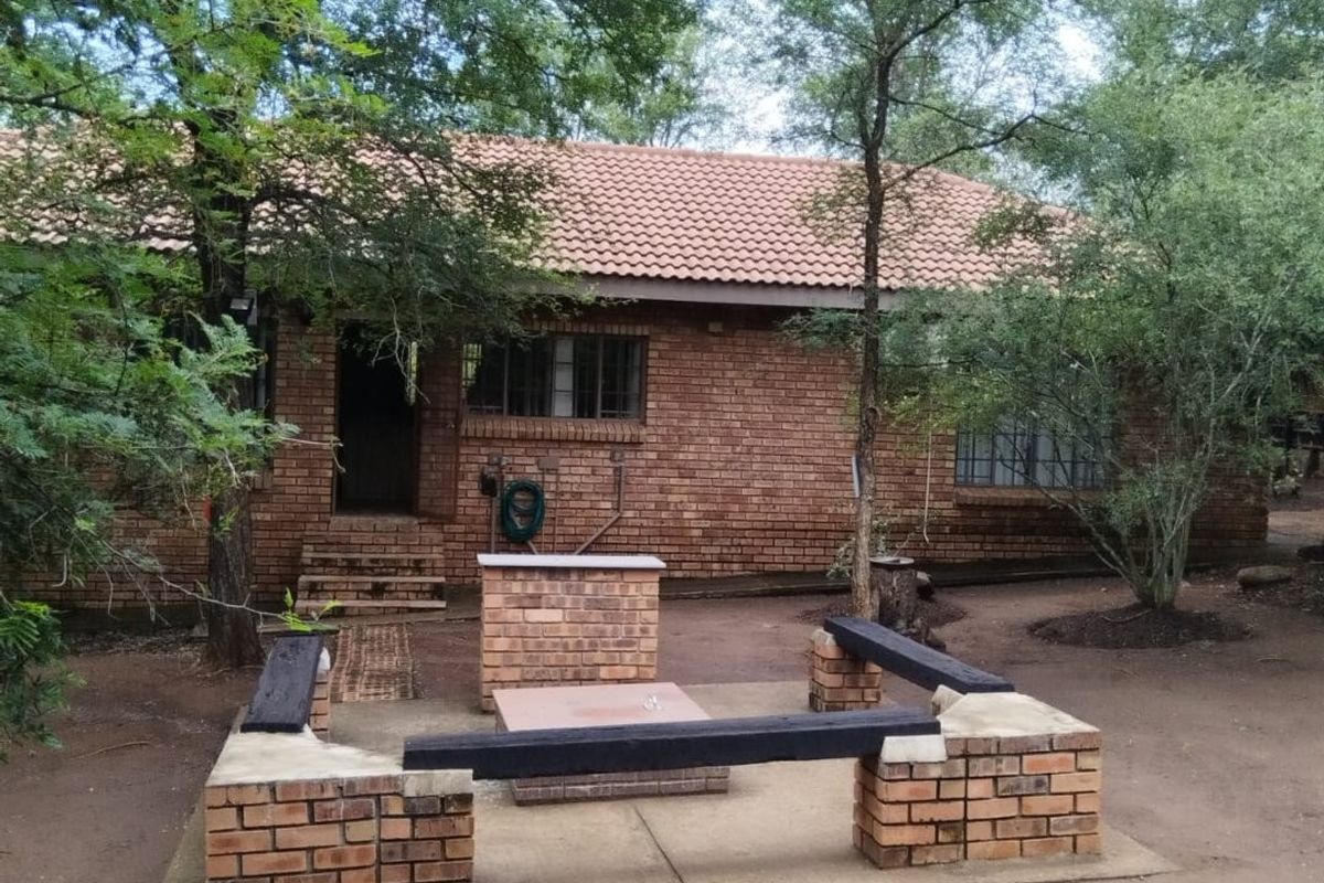 Rear exterior view of a brick house featuring a built-in brick braai and integrated seating area set within a garden space.