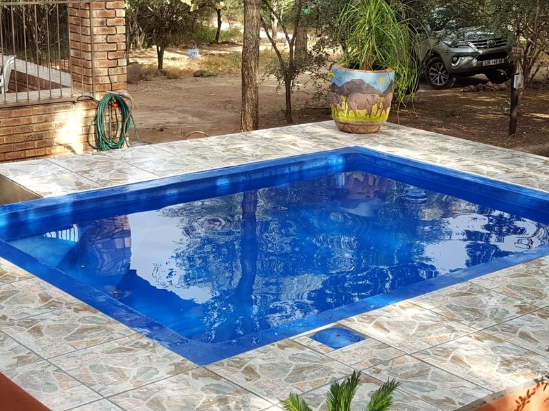 A rectangular swimming pool featuring a tiled surround and adjacent brick pillar structure, set within a natural outdoor environment.