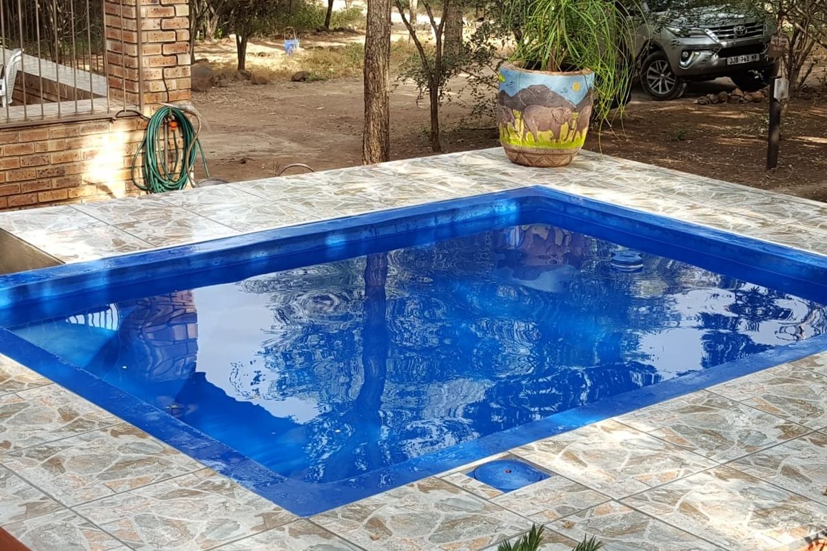 A rectangular swimming pool featuring a tiled surround and adjacent brick pillar structure, set within a natural outdoor environment.