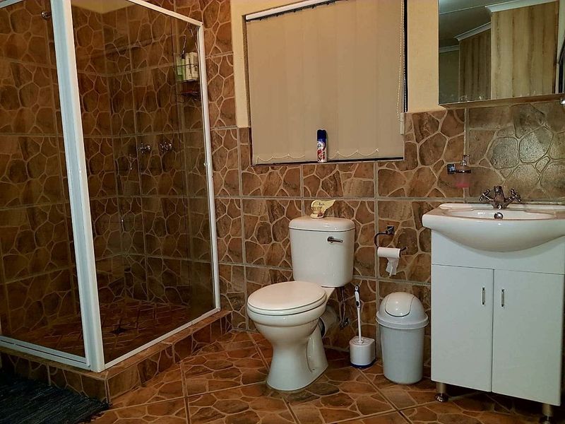 A functional bathroom featuring a shower enclosure, toilet, and vanity basin with dated stone-look wall and floor tiling.