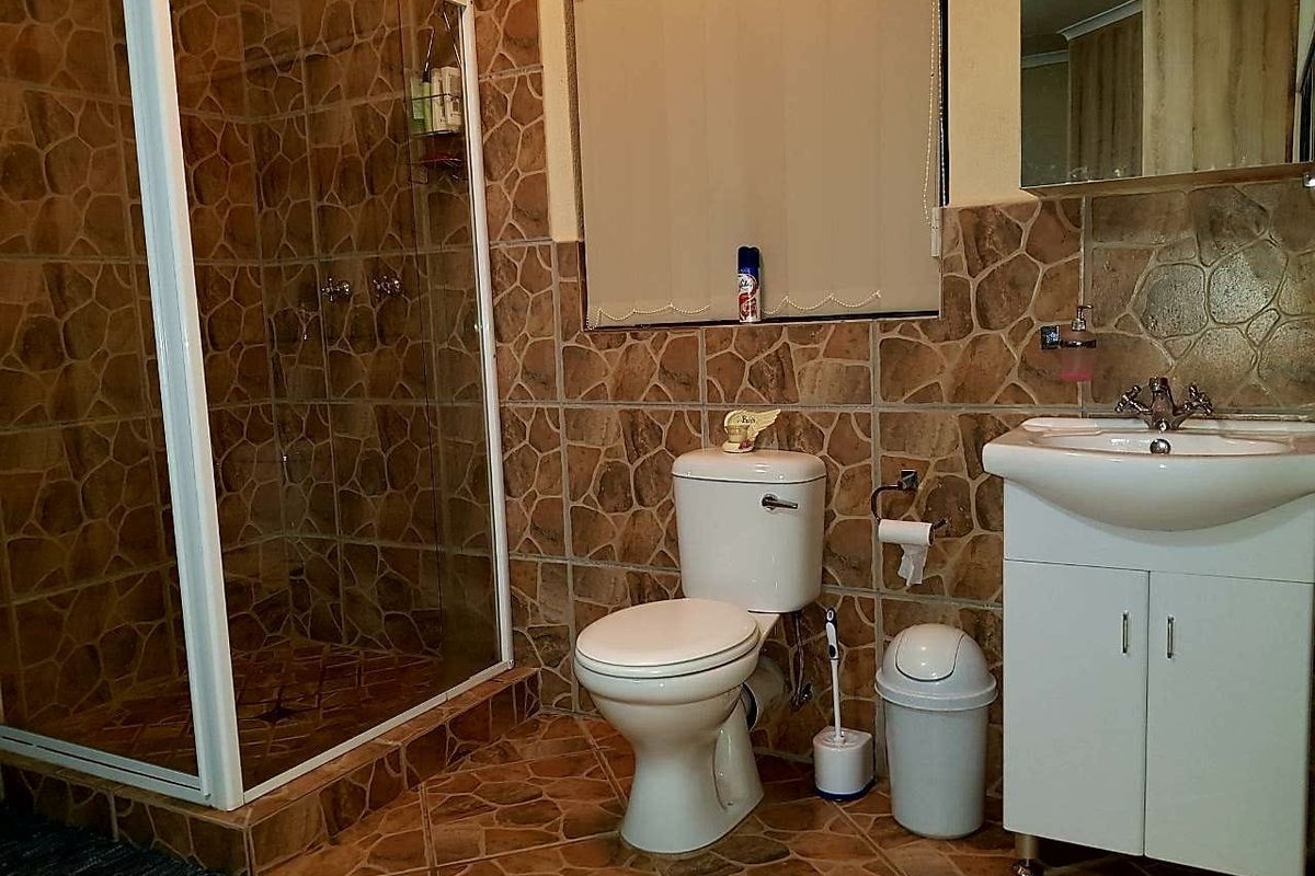A functional bathroom featuring a shower enclosure, toilet, and vanity basin with dated stone-look wall and floor tiling.