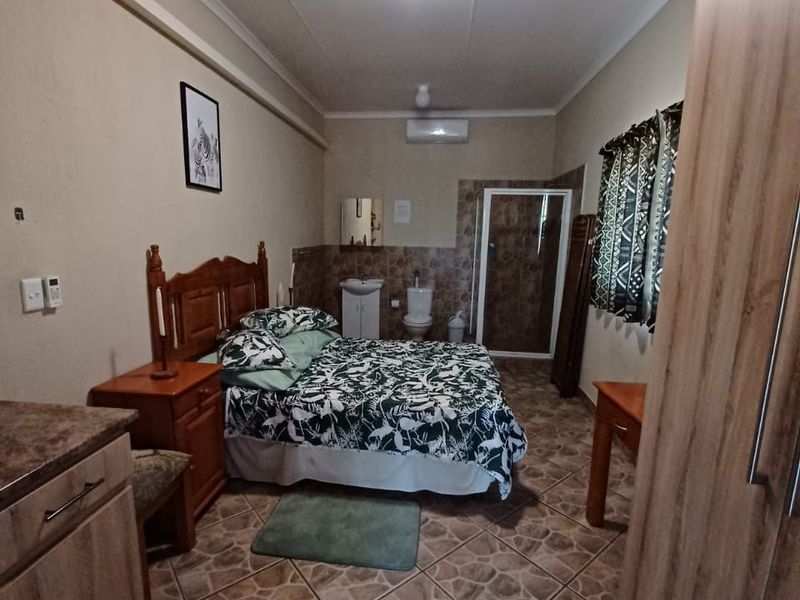 A bedroom featuring tiled flooring, an en-suite bathroom with a shower, and a wall-mounted air conditioning unit.