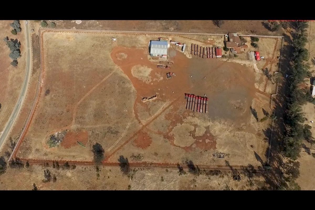 Aerial view of a large industrial property featuring a warehouse shed, extensive open yard space, and perimeter fencing.