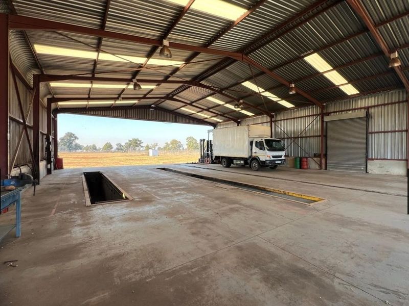 Spacious industrial workshop featuring a high-clearance corrugated metal roof, integrated inspection pits, and a large roller shutter door for vehicle access.