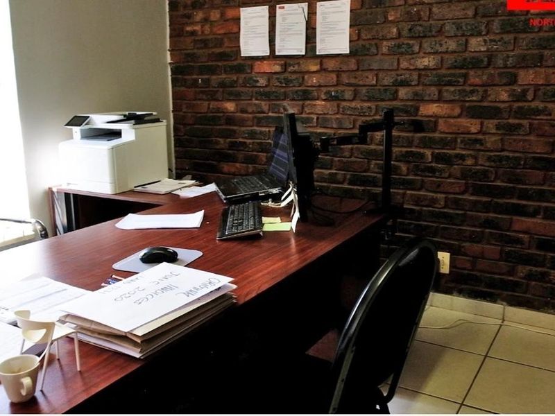 A functional office space featuring an exposed brick feature wall and tiled flooring, providing a professional industrial aesthetic.