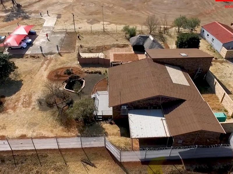 Aerial view of the industrial property featuring a main building, carport, thatched lapa, and secure perimeter fencing with razor wire.