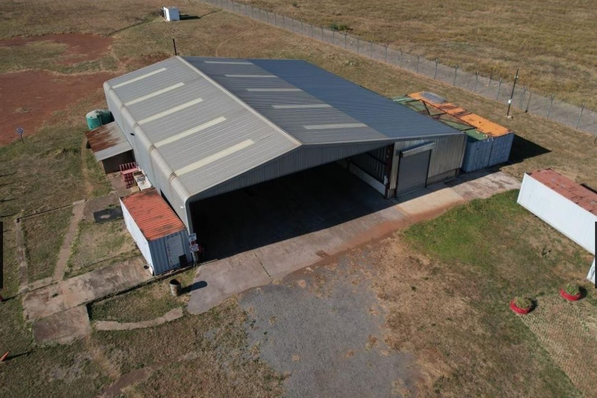 Aerial view of an industrial warehouse facility featuring a large open-span portal frame structure, corrugated metal cladding, and a concrete apron.