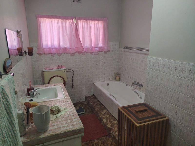 A dated bathroom featuring a built-in tiled vanity, inset basin, and a sunken bathtub with classic wall tiling.