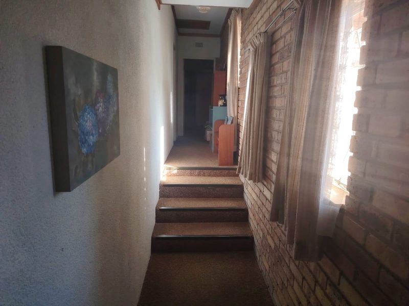 A hallway featuring exposed brick walls and carpeted stairs leading to an upper level, showing signs of age and wear.
