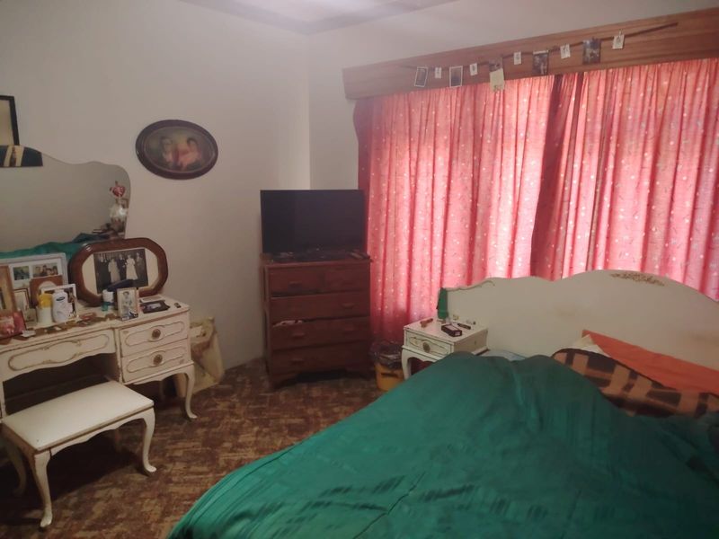 A bedroom featuring a curtain pelmet and carpeted flooring, currently presented with dated finishes and personal decor.