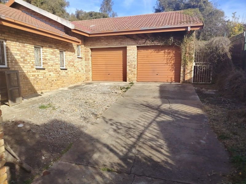 Exterior view of a double garage with a brick facade, tiled roof, and a concrete driveway requiring maintenance and landscaping.