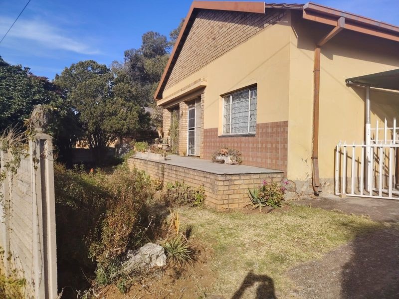 Front elevation of a single-story brick house featuring a raised porch, security gates, and metal window bars, set within a garden area.