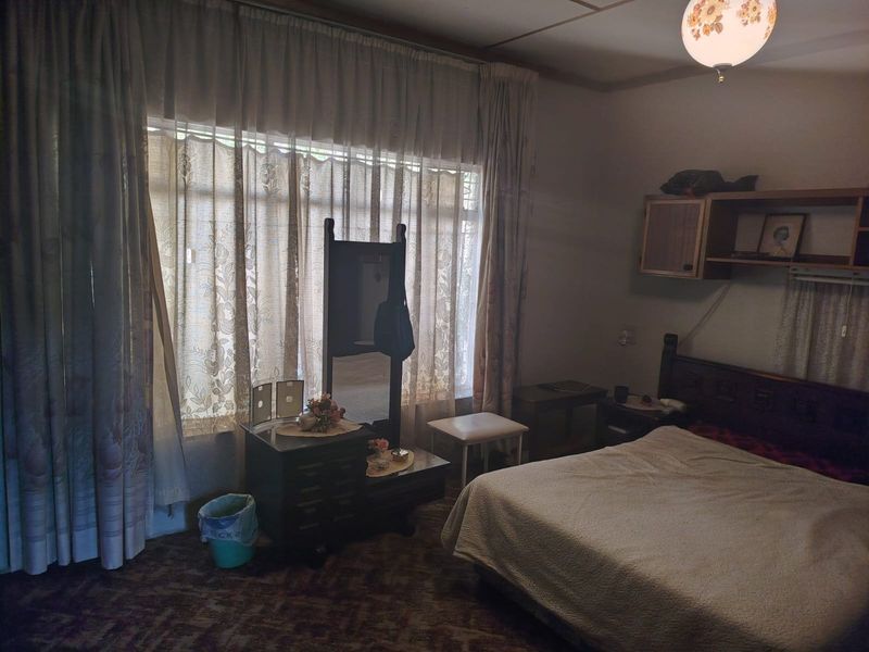 A bedroom featuring a large window with curtains and built-in wall shelving, requiring cosmetic updates to the flooring and finishes.