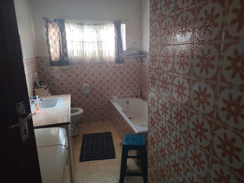 A dated bathroom featuring a built-in bathtub, vanity basin, and toilet, finished with traditional patterned wall tiles.