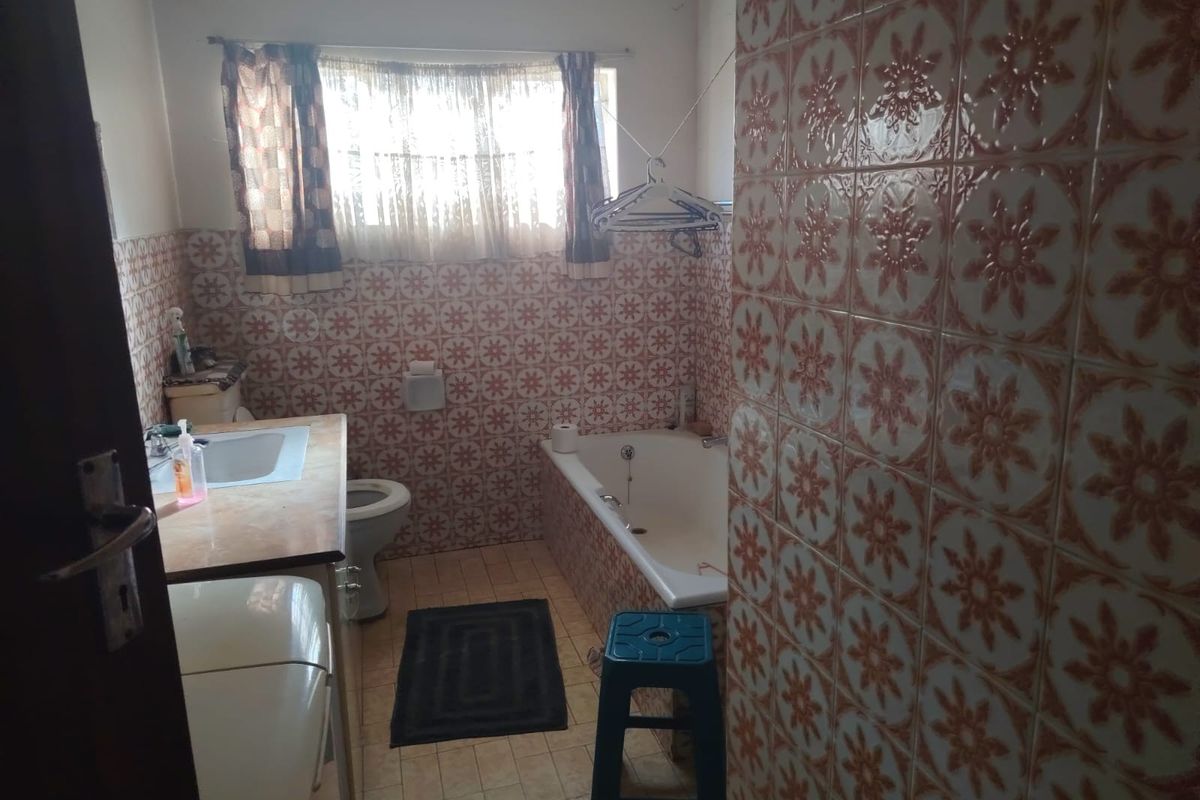 A dated bathroom featuring a built-in bathtub, vanity basin, and toilet, finished with traditional patterned wall tiles.