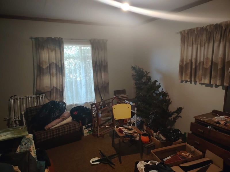 A bedroom space featuring carpeted flooring and window treatments, currently used for storage and in need of cosmetic updates.