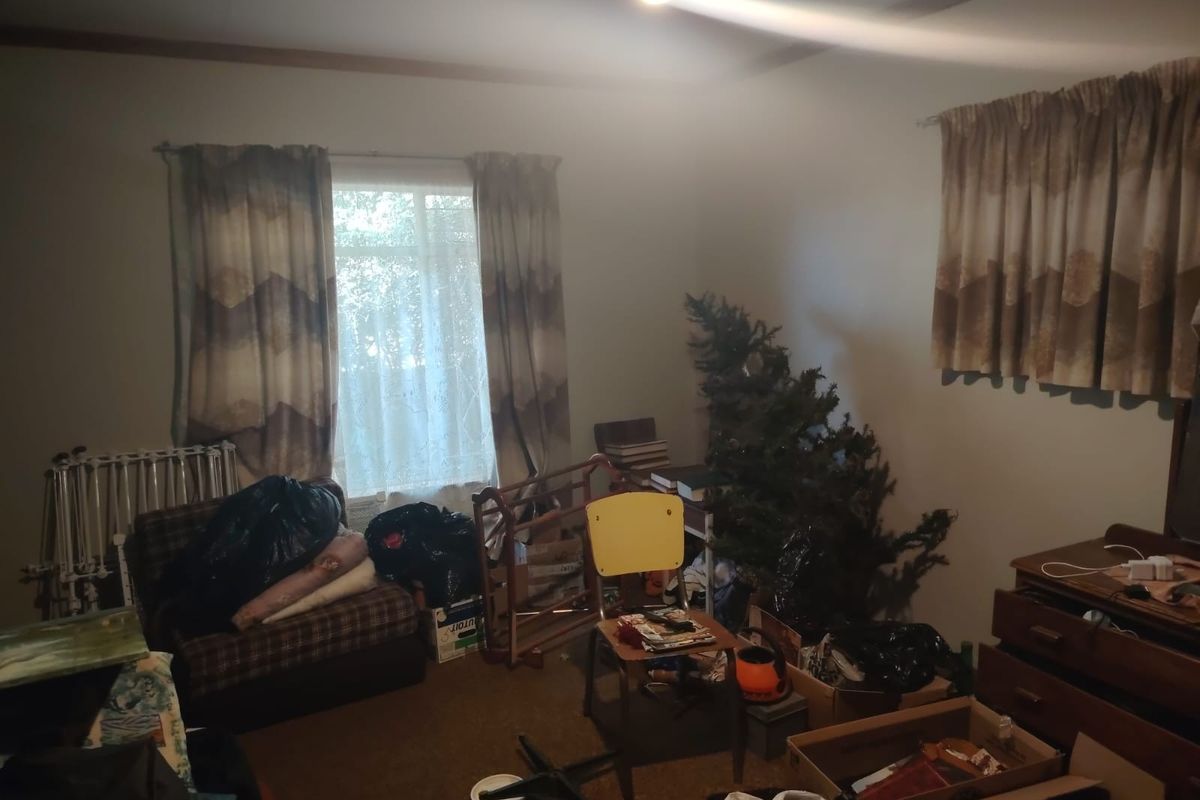 A bedroom space featuring carpeted flooring and window treatments, currently used for storage and in need of cosmetic updates.
