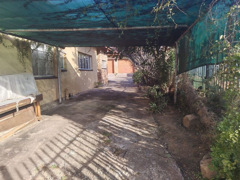 A driveway leading to a brick garage, featuring a covered carport area with shade cloth and concrete paving.