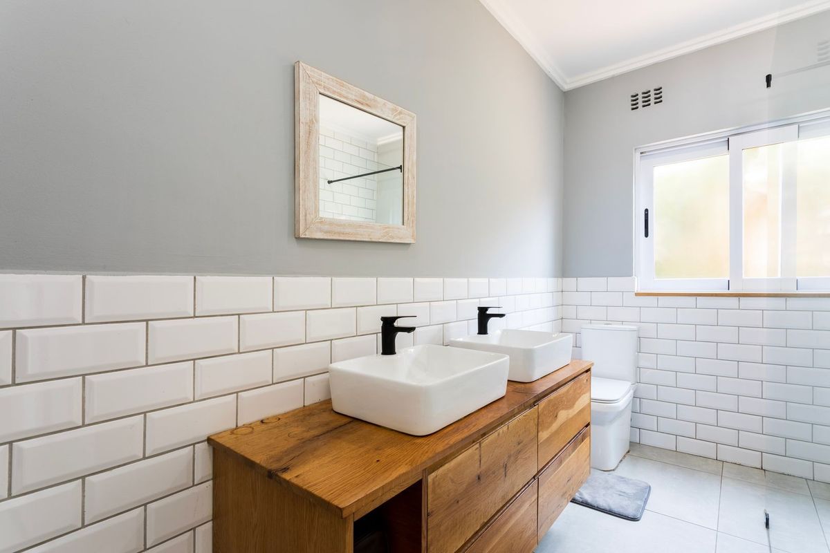 Modern bathroom featuring a double vanity with timber cabinetry, vessel sinks, black fixtures, and classic white subway tile backsplash.