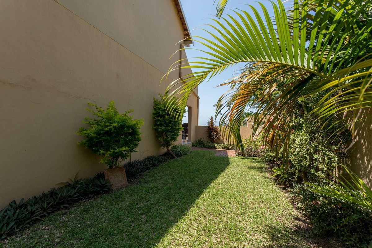 A well-maintained rear garden area featuring a manicured lawn, paved pathway, and perimeter boundary wall.