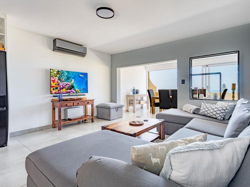 An open-plan living area featuring tiled flooring, a wall-mounted air conditioning unit, and direct access to an adjoining balcony space.