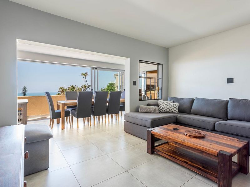 Spacious open-plan living and dining area featuring large sliding doors leading to a balcony with ocean views and neutral tiled flooring.