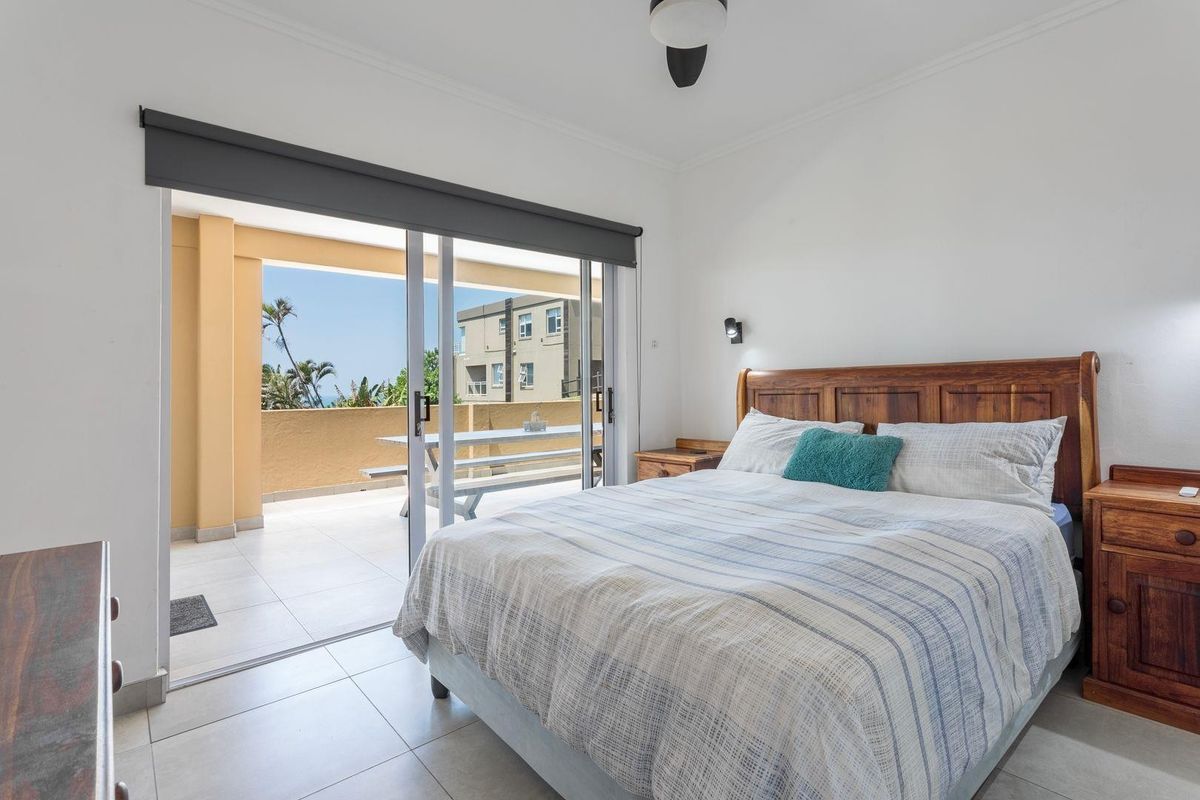 A bright bedroom featuring tiled flooring and large sliding glass doors that open onto a private balcony.