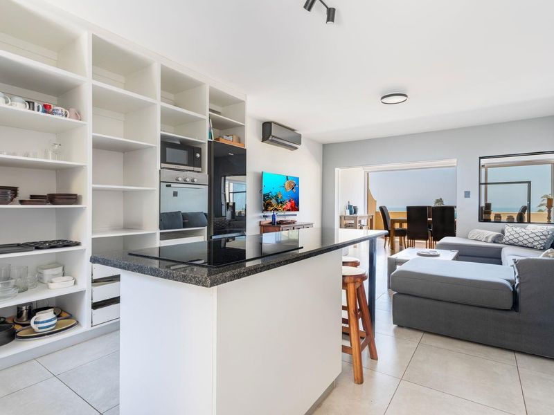 Modern open-plan living area featuring a sleek kitchen island with integrated appliances, extensive built-in shelving, and seamless flow to the outdoor balcony space.