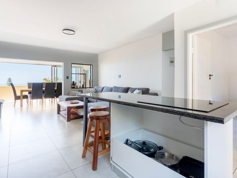 Spacious open-plan living and kitchen area featuring a modern island with a built-in cooktop, tiled floors, and seamless access to a balcony with views.