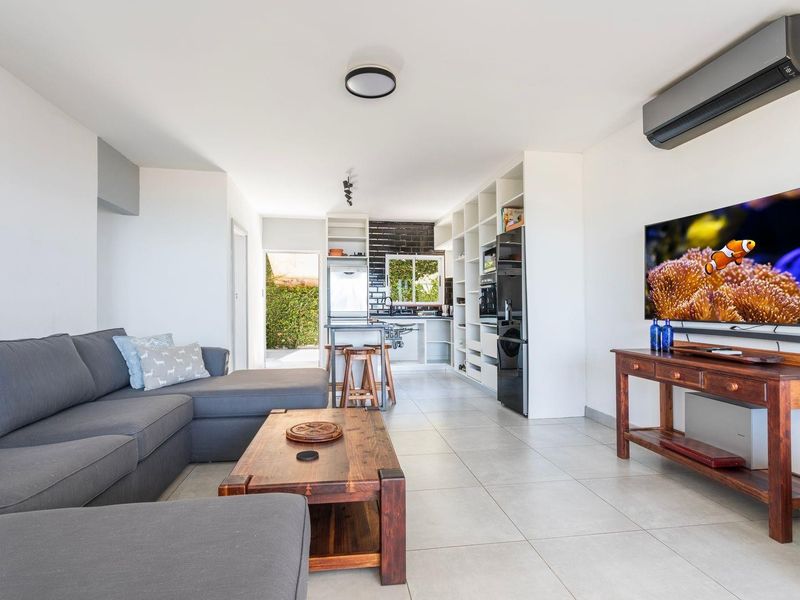 An open-plan living and kitchen area featuring tiled floors, built-in shelving, modern cabinetry, and a split-system air conditioner.