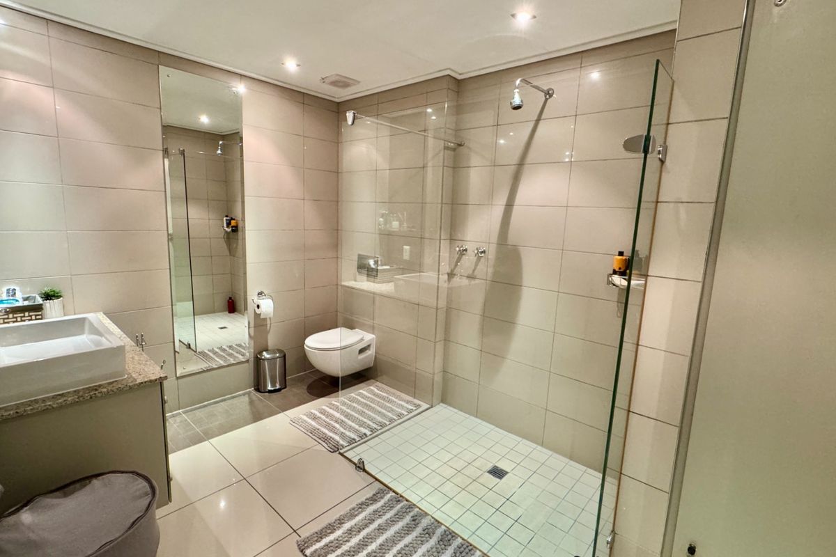 Modern bathroom featuring a wall-mounted toilet, a spacious walk-in shower with a frameless glass screen, and a vanity with a granite countertop.