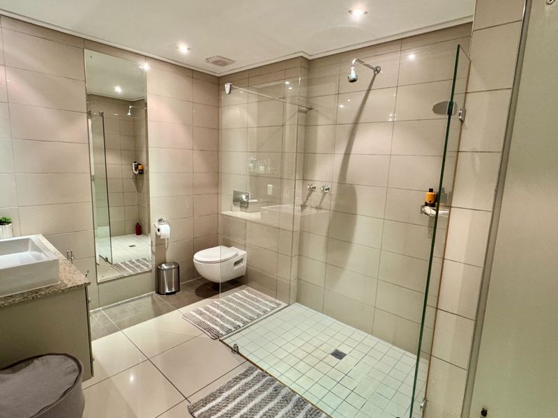 Modern bathroom featuring a wall-mounted toilet, a spacious walk-in shower with a frameless glass screen, and a vanity with a granite countertop.