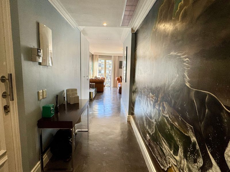 A spacious, well-lit hallway featuring polished concrete floors, decorative wall mural, and integrated ceiling lighting leading towards the main living area.