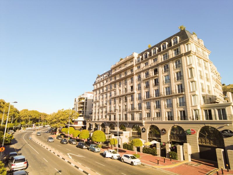 A high-angle view of a multi-story apartment building facade featuring classic architectural details, balconies, and ground-level commercial spaces along a street.