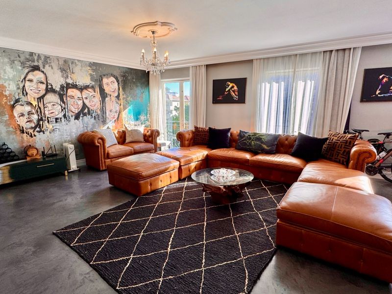Spacious living room featuring polished concrete floors, decorative ceiling cornicing, and a central chandelier, creating a modern and well-maintained living space.