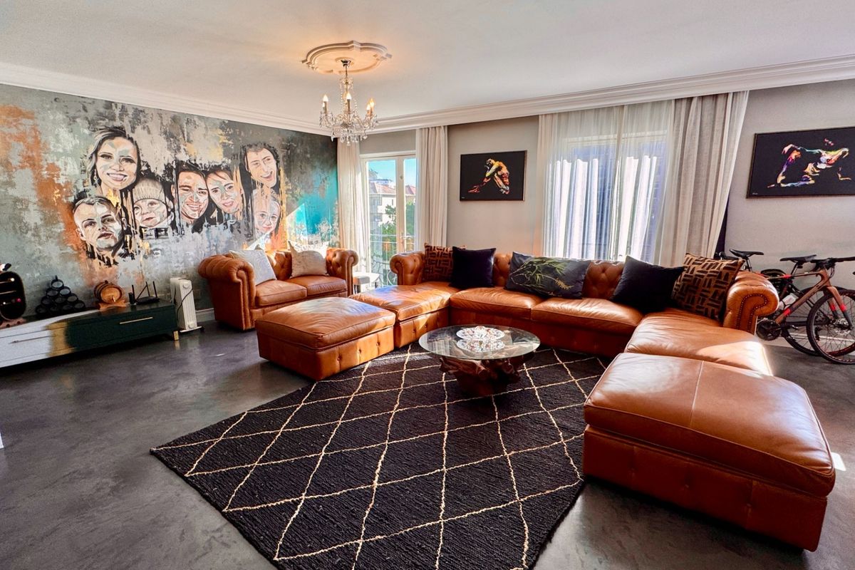 Spacious living room featuring polished concrete floors, decorative ceiling cornicing, and a central chandelier, creating a modern and well-maintained living space.