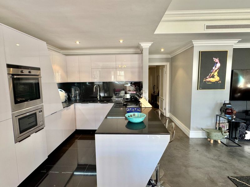Modern open-plan kitchen featuring high-gloss cabinetry, integrated appliances, a sleek kitchen island with stone countertops, and recessed lighting, seamlessly flowing into the living area.