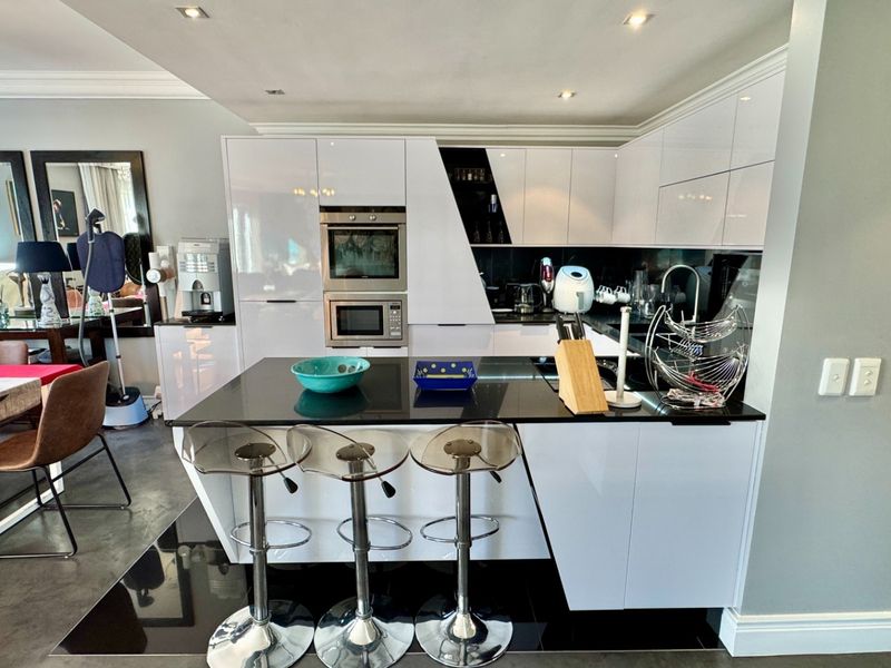 Modern open-plan kitchen featuring high-gloss white cabinetry, black stone countertops, and integrated appliances, seamlessly flowing into the adjacent dining area.